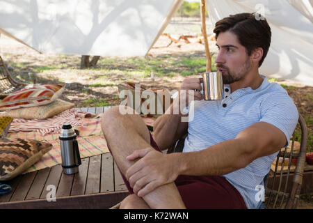 Thoughtful young man drinking coffee in tent Stock Photo