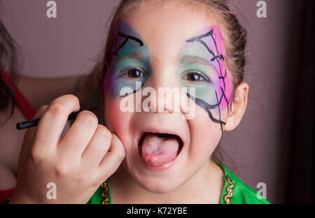 Little girl with tongue out while she is made up by make-up artist Stock Photo