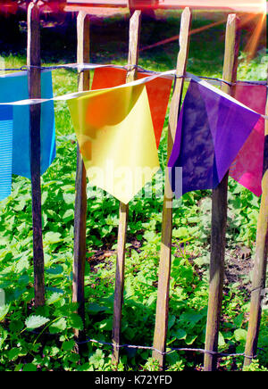 Multi-colored bunting flags on a wooden fence with light flare from the sun Stock Photo