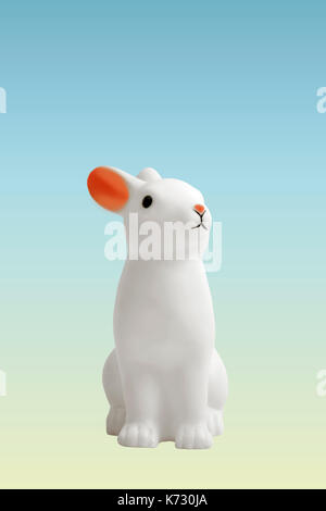 a cute white plastic bunny on a pastel gradient blue and yellow background. Minimal color still life photography Stock Photo