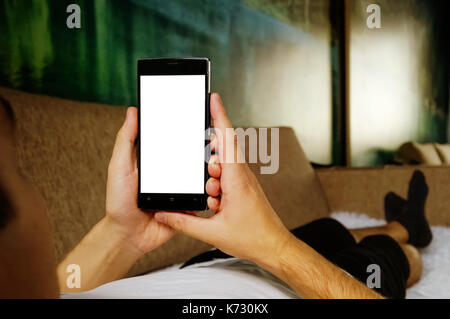 Man relaxing during looking at the screen while lying on sofa - blank screen smartphone Stock Photo