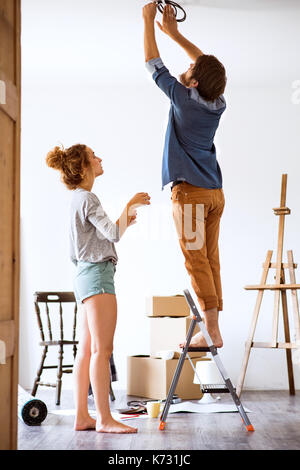 Young couple moving in new house, changing a light bulb. Stock Photo