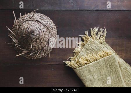 Beige carpet with fringe and straw hat in Bali style on dark wooden floor, texture close up Stock Photo