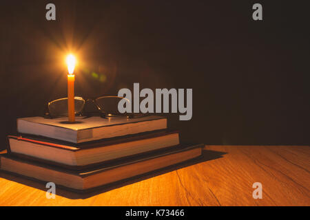 Close-up of burning candle with pile of old book on wooden table. Education concept. Stock Photo