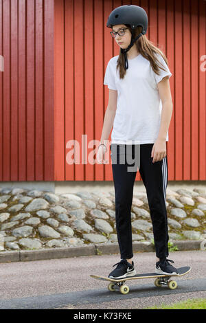Teenage girl with protective skateboard helmet skateboarding outdoors  Model Release: Yes.  Property Release: No. Stock Photo