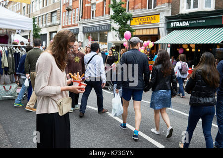 Woman on mobile phone cellphone texting whilst eating churros food on a London street with people UK Stock Photo