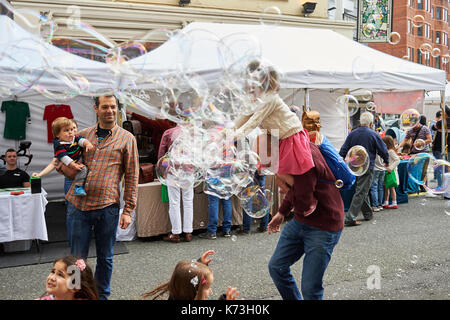 Children and adults parents playing with bubbles having fun on a London street fair fayre UK Britain Stock Photo