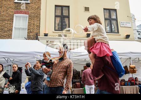 Children and adults parents playing with bubbles having fun on a London street fair fayre UK Britain Stock Photo