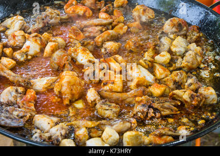 Pieces of rabbit and chicken meat frying with tomato sauce in olive oil in large flat pan. Cooking paella or jambalaya on gas burner. Outdoors, picnic Stock Photo