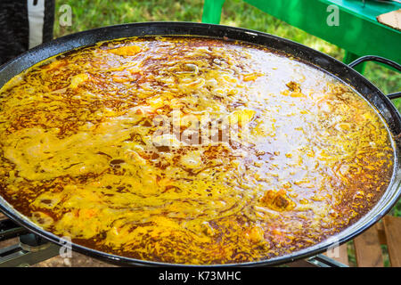 Process of cooking Spanish paella or jambalaya in large flat frying pan. Ingredients meat, rice, vegetables, spices simmering in broth with tomato sau Stock Photo