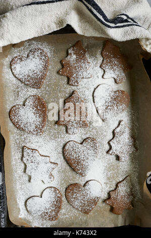 Kitchen photo of a dusted wooden chopping board and antiqued t-towel with uncooked, prepared, cookie dough cut into festive shapes for Christmas. Stock Photo