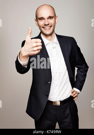 Happy young businessman shows his thumb. Studio shot on gray background. Stock Photo