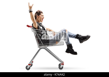 Punk girl riding in a shopping cart and making a rock hand gesture isolated on white background Stock Photo