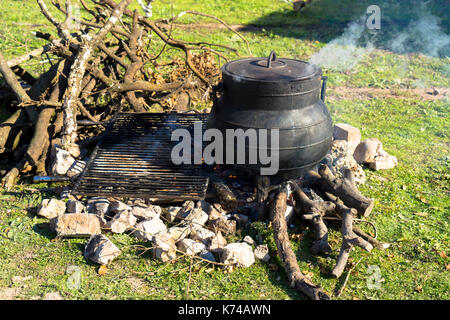 Cooking over an open fire using a metal cooking pot gently steaming on a wood burning campfire Stock Photo