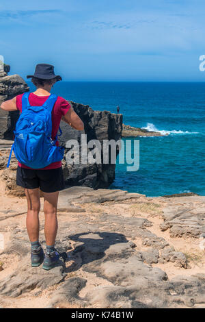 A female hiker standing on the clifftop looking out to sea along the Fishermans Trail near Vila Nova de Milfontes Portugal. Lone angler in the distance Stock Photo