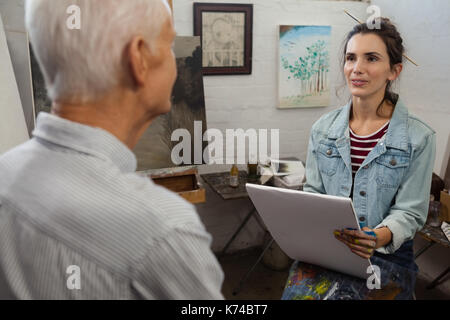 Woman interacting with senior man while sketching on canvas in drawing class Stock Photo