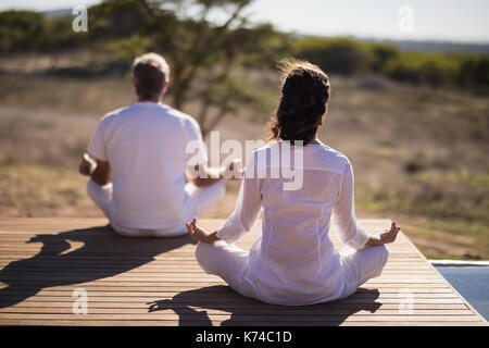 Rear view of couple practicing yoga on wooden plank on a sunny day Stock Photo