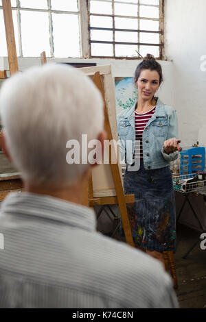 Woman interacting with senior man while painting on canvas in drawing class Stock Photo