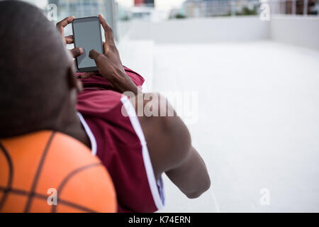 Basketball player using mobile phone while relaxing on terrace Stock Photo
