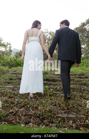 Rear view of newlywed couple walking on grassy field in forest Stock ...