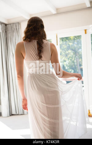 Rear view of young bride in wedding dress standing at home Stock Photo