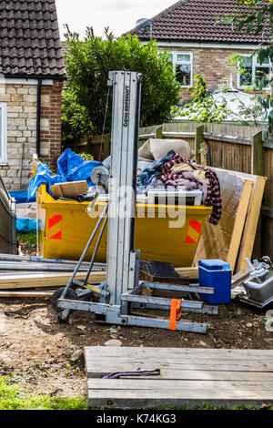 A large hired skip in the garden of a house, full of waste materials relating to a household building project. England, UK. Stock Photo