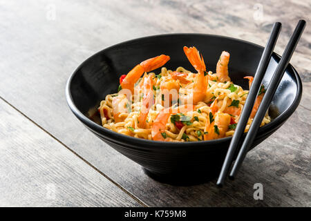 Noodles and shrimps with vegetables in black bowl on wooden table Stock Photo