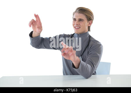 Smiling male doctor touching imaginary interface screen while sitting at table against white background Stock Photo