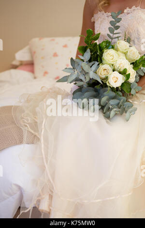 Midsection of bride in wedding dress holding bouquet while sitting on bed Stock Photo