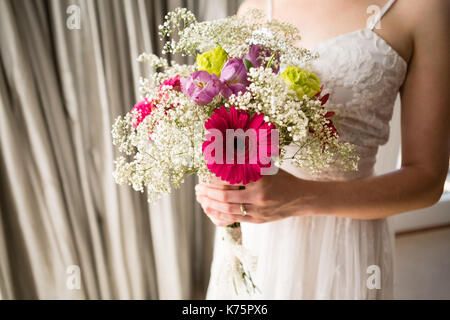 Midsection of bride in wedding dress holding bouquet while standing at home Stock Photo