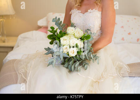 Midsection of bride in wedding dress holding bouquet while sitting on bed at home Stock Photo