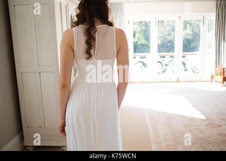 Rear view of bride in wedding gown standing at home Stock Photo
