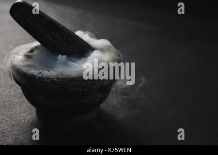 Smoke in pestle and mortar on black surface Stock Photo