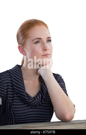 Thoughtful businesswoman with hand on chin sitting at table against white background Stock Photo