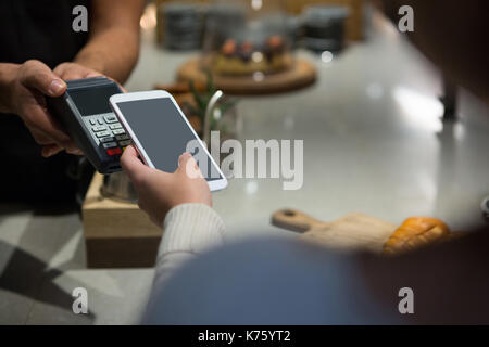 Woman paying bill through smartphone using NFC technology in restaurant Stock Photo