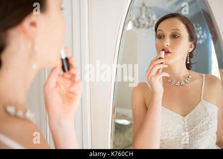 Side view of beautiful bride applying lipstick reflecting on mirror at home Stock Photo