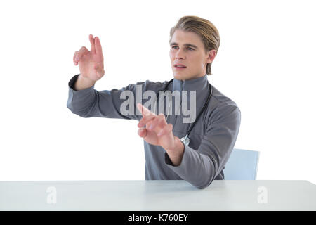 Male doctor touching imaginary interface screen while sitting at table against white background Stock Photo