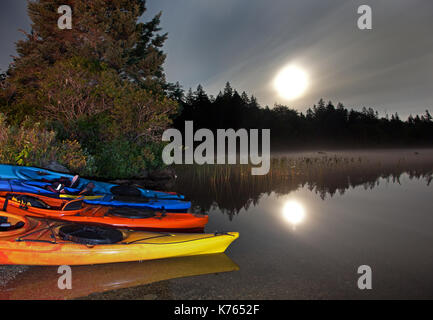 moonlight reflecting in a lake with kayaks by the shoreline Stock Photo