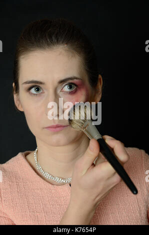 Home violence. Beaten woman trying to cover her injuries by make-up brush. Stock Photo