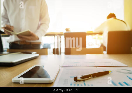 Image of business documents on workplace with two partners interacting on background. Stock Photo