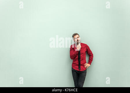 Thinking people . Young adult bearded worker touching chin, thinking and looking up. Studio shot. Isolated on gray background. Stock Photo