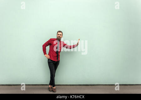 Business person in red shirt, tie and black casual trousers, standing on gray wall and prop something invisible. Outdoor Stock Photo