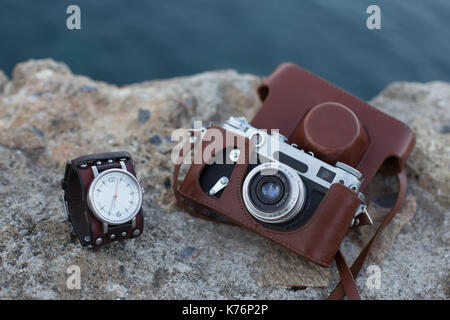 Old vintage film camera in brown leather case and watch with leather bracelet placed on stone  surface Stock Photo