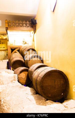 A variety of different wooden barrels are lying on the brick floor near the wall of the winehouse. Stock Photo