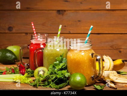 Assortment of fruit and vegetable smoothies in glass jars with straws on wooden background. Stock Photo