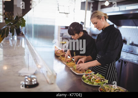 Young female chefs preparing fresh food at kitchen counter in cafeteria Stock Photo