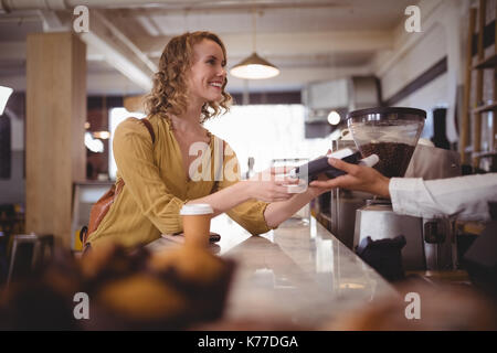 Smiling beautiful female customer paying through card at counter in coffee shop Stock Photo