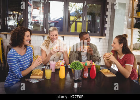 Smiling young friends eating food while sitting at table in coffee shop Stock Photo