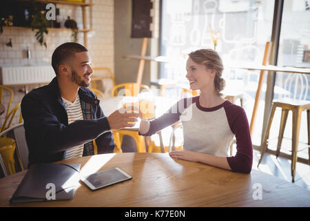 Smiling young friends raising toast with juice while sitting at table in coffee shop Stock Photo