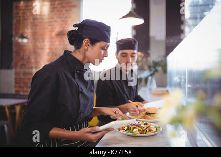 Young wait staff discussing over food with digital tablet and clipboard at counter in coffee shop Stock Photo